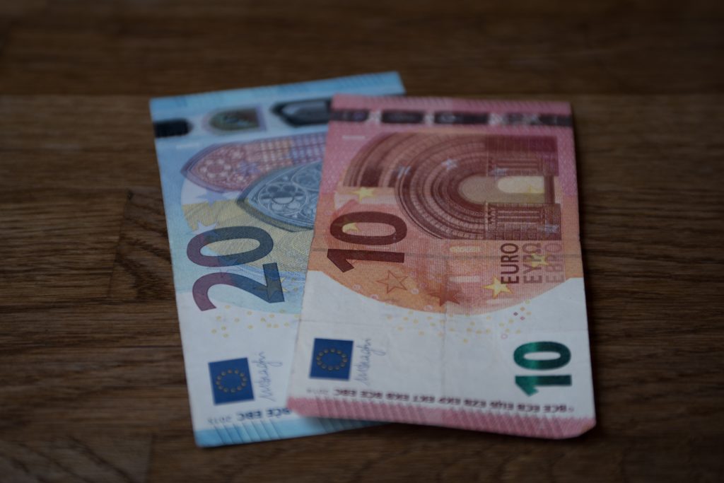 A 20 euro bill and a 10 euro bill are stacked on a brown tabletop.